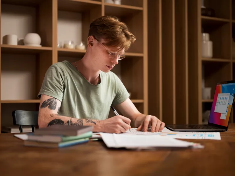 Young man writing notes at a wooden desk; associated with Fantastic Writing Tips and How to Find Them.
